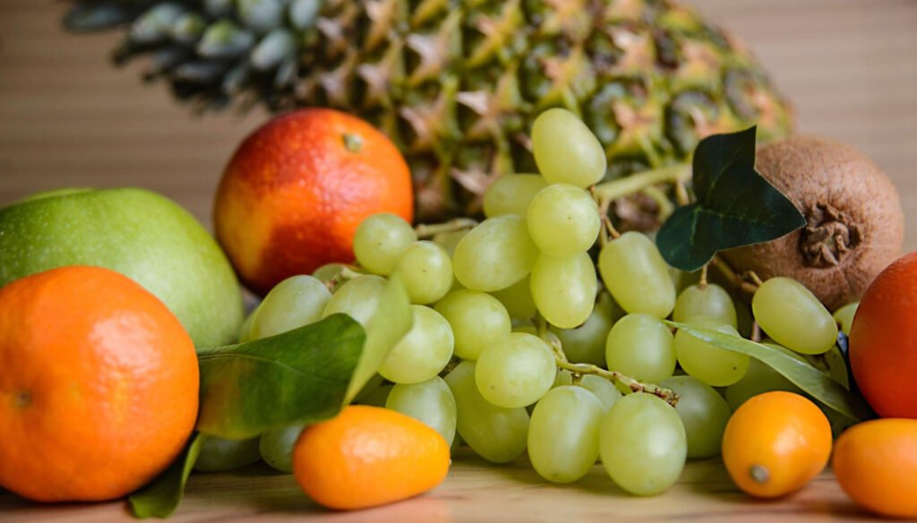 Fruits variés avec raisins verts, mandarines, kiwi et ananas en arrière-plan.
