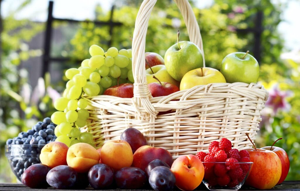 Corbeille en osier remplie de raisins, pommes, et autres fruits dans un jardin ensoleillé.