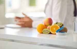 Un assortiment de fruits frais, dont des oranges, des pommes et des kiwis, accompagné d'un mètre ruban bleu, sur une table blanche.