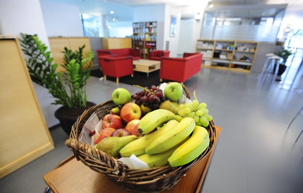 Corbeille de fruits avec bananes, raisins, pommes, et poires dans un espace bureau.