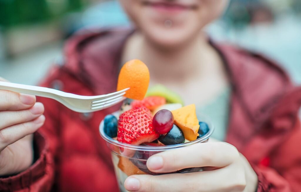 Une personne dégustant une salade de fruits frais avec une fourchette en plastique.